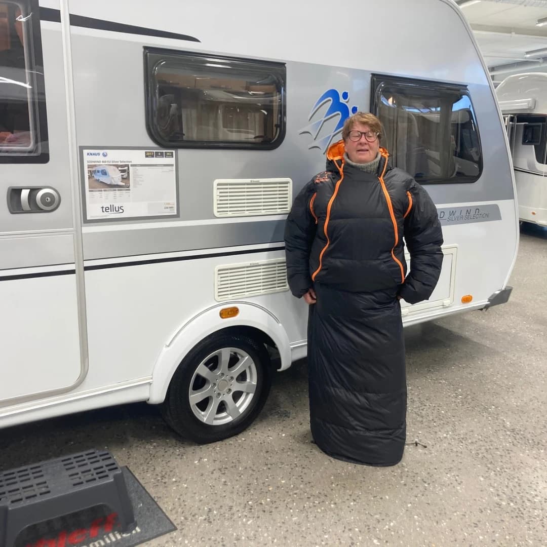 Besøkende prøver et svart Utekos-plagg med oransje detaljer ved en campingvogn